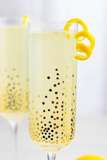A French 75 cocktail in a sparkling, golden glass with fruit peel garnish on rim