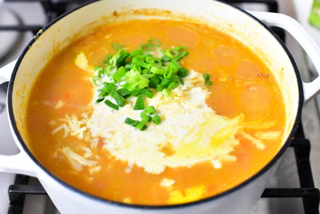 fresh scallions and heavy cream being added to pot of ham and potato soup