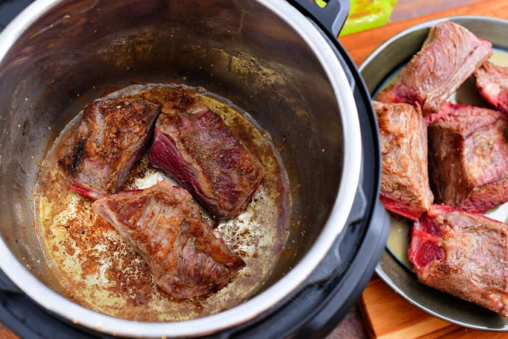 searing pieces of beef in an electric pressure cooker