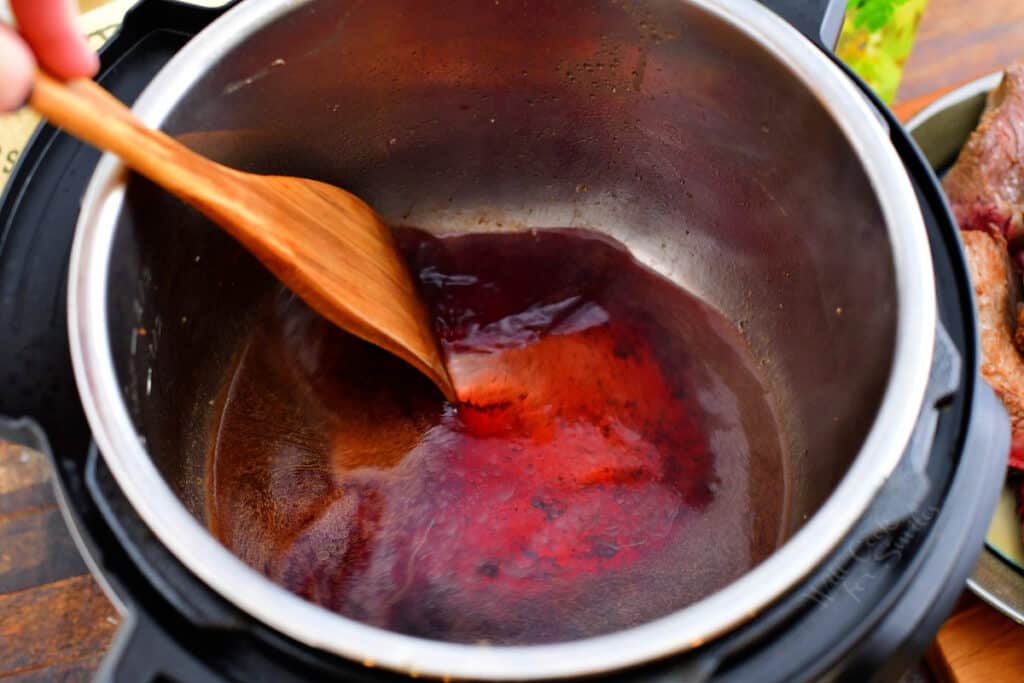 A wooden spoon is stirring red wine in large pot.