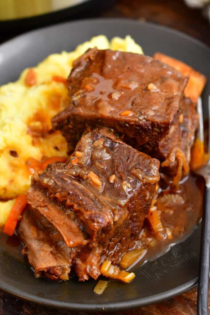 Two pieces of short rib sit on top of a helping of mashed potatoes.