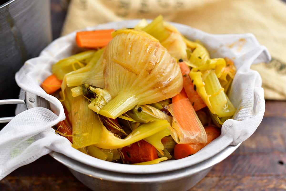 cooked onions, celery and carrots in a cheesecloth lined strainer