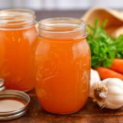 vegetable broth in two canning jars next to fresh carrots, garlic, and celery