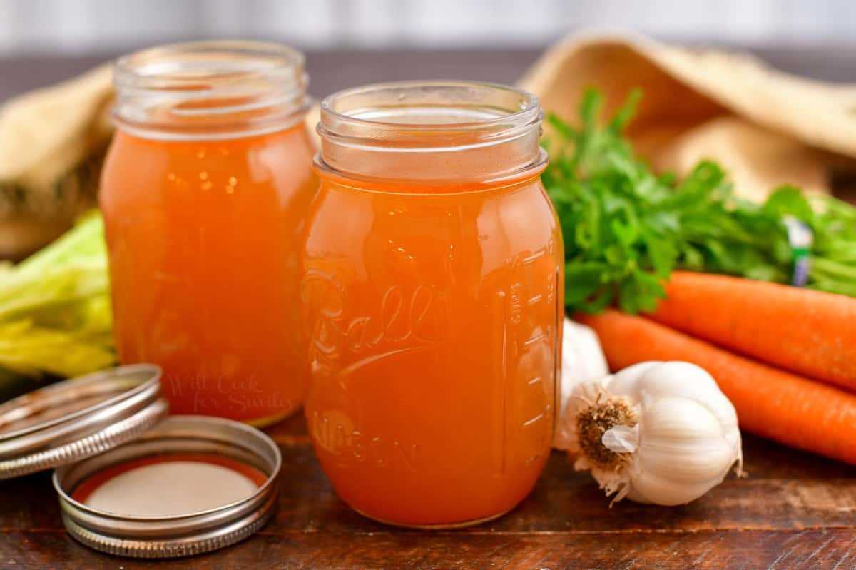 vegetable broth in two canning jars next to fresh carrots, garlic, and celery