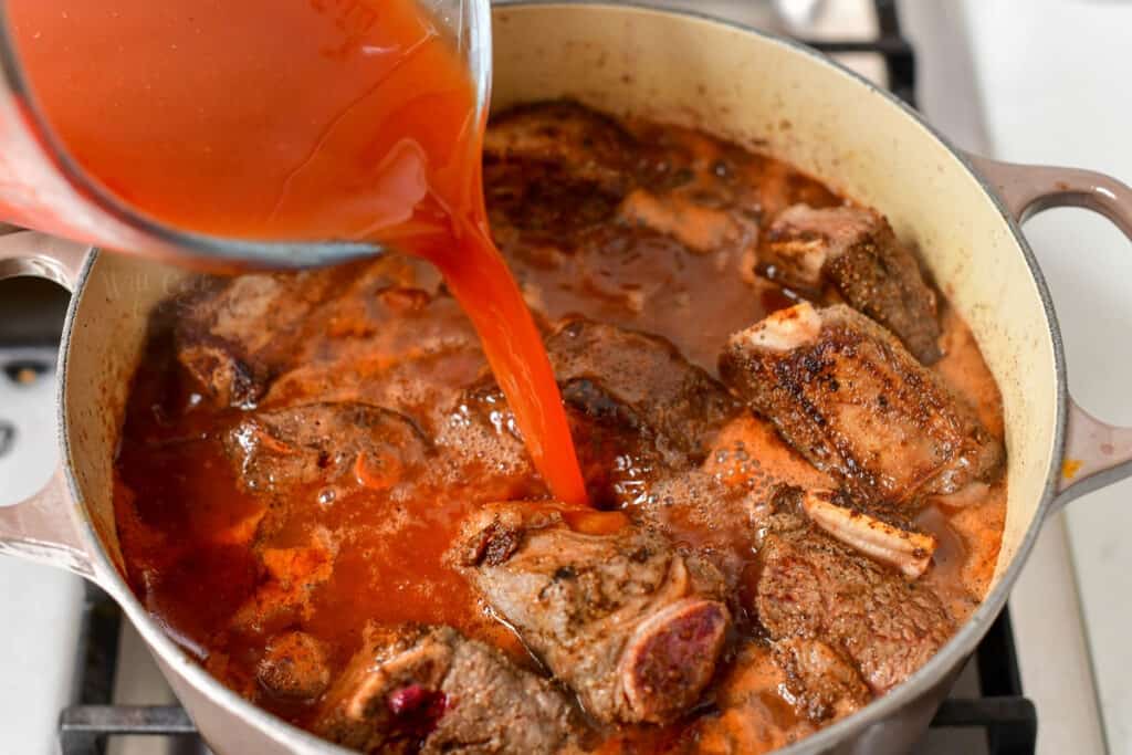 pouring stock into a large pot with braised beef ribs