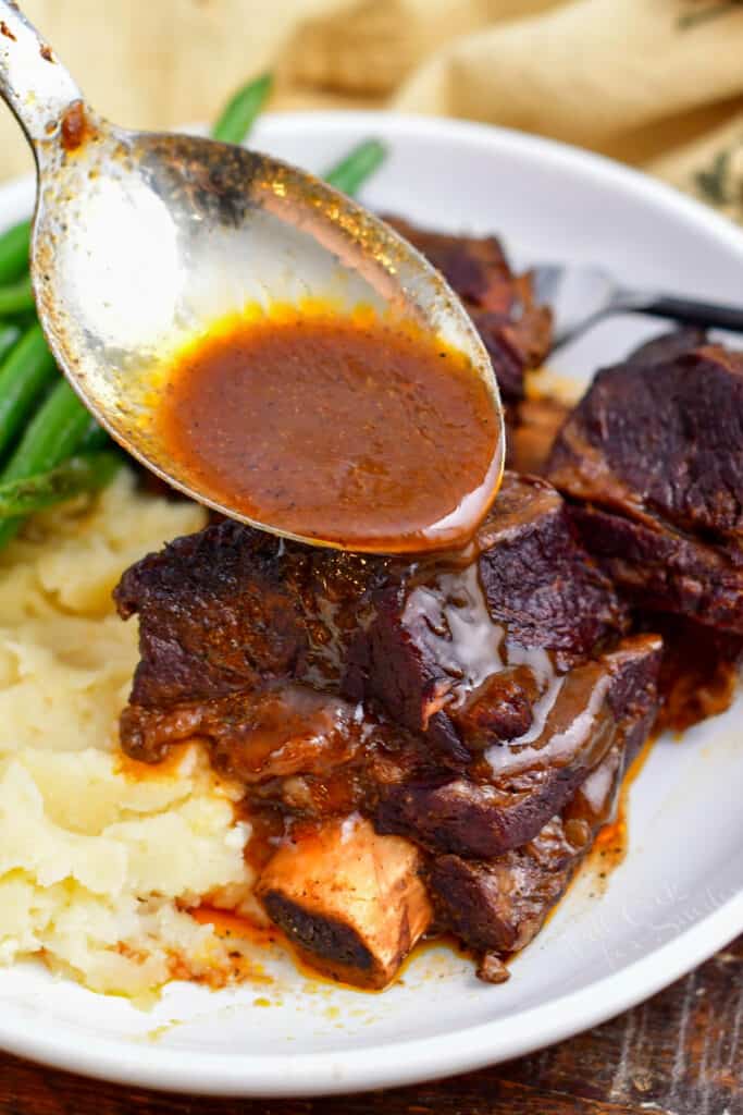 closeup: spooning sauce over plate of braised short ribs and mashed potatoes