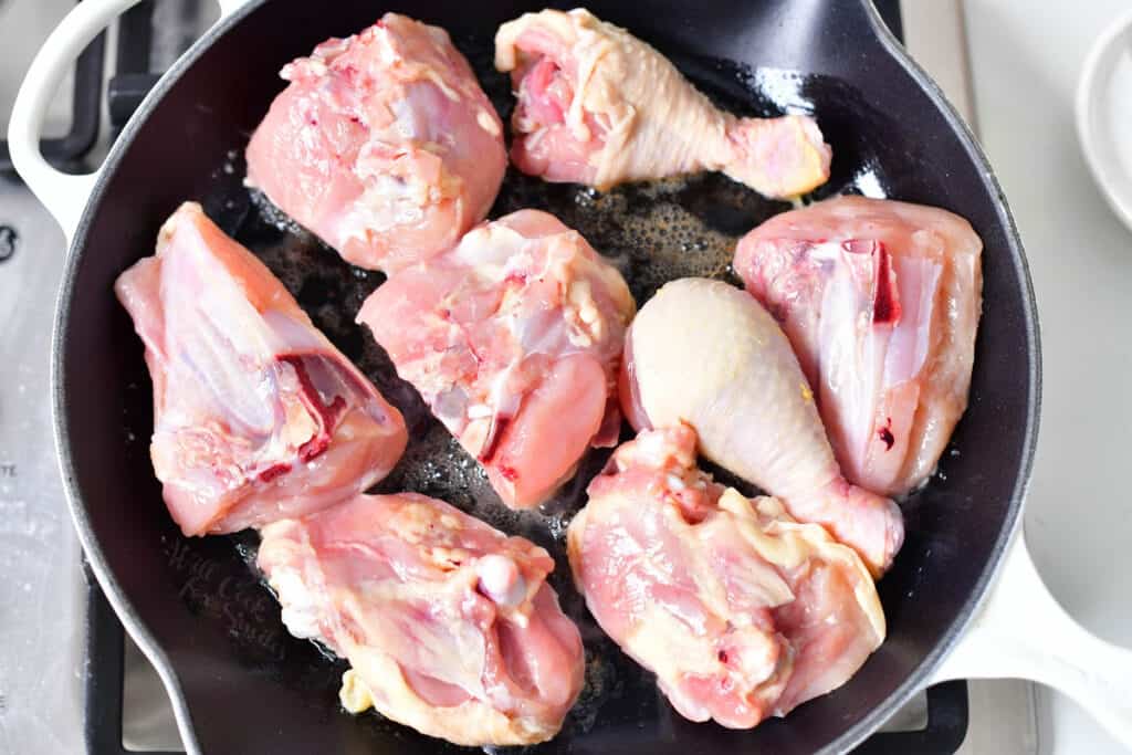 raw pieces of bone-in chicken in frying pan of oil