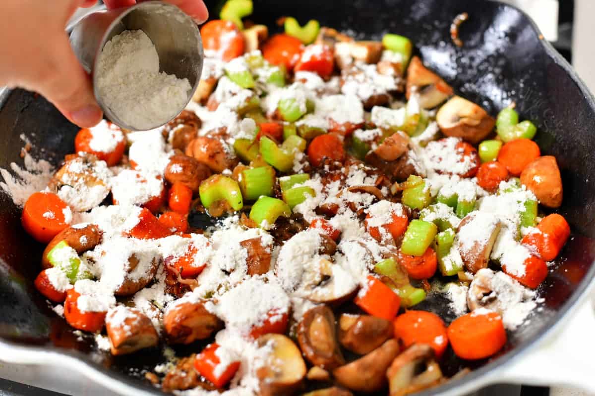 adding white flour to pan of cooked vegetables to make a roux