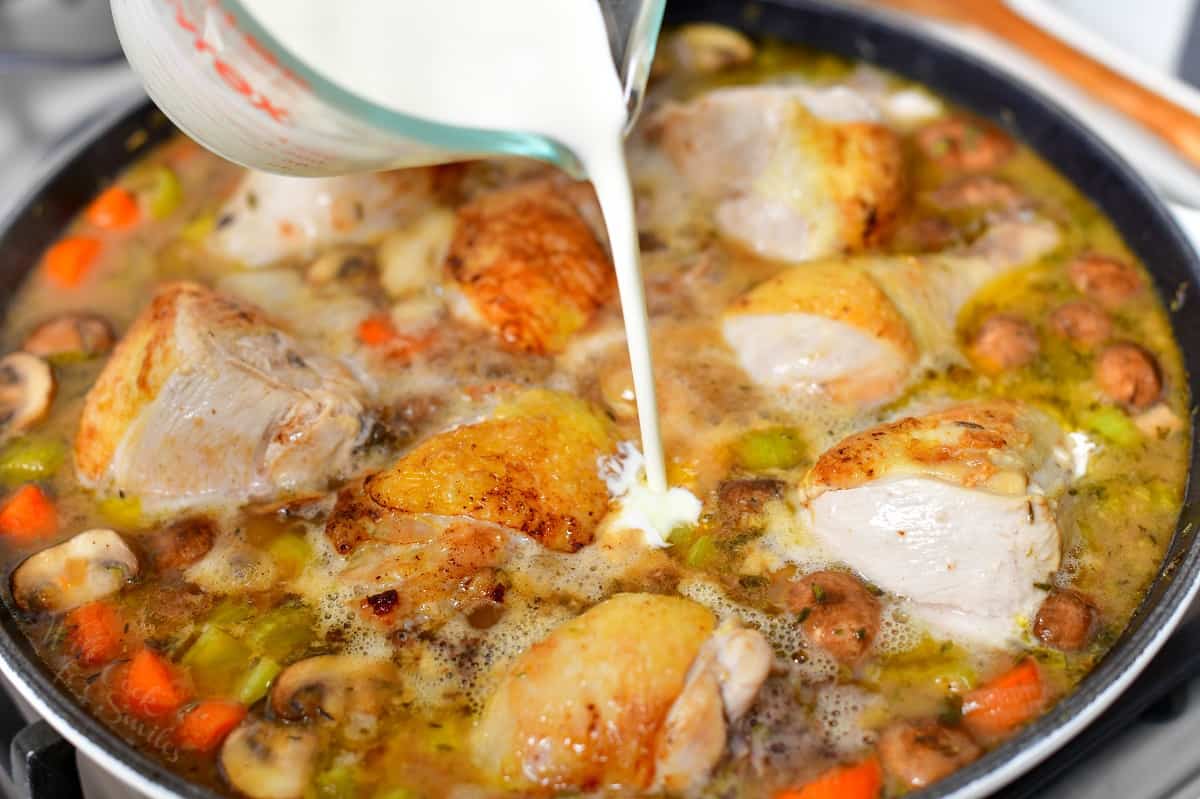 pouring heavy cream into skillet of cooked chicken stew