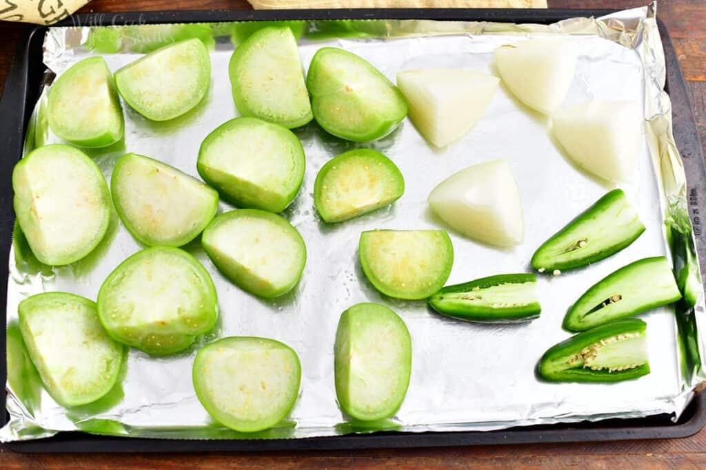 halved tomatillos and jalapenos with quartered onions on a foil lined baking sheet