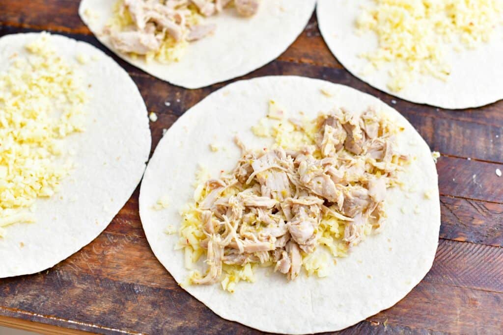 tortillas on a wooden surface filled with cheese and shredded chicken