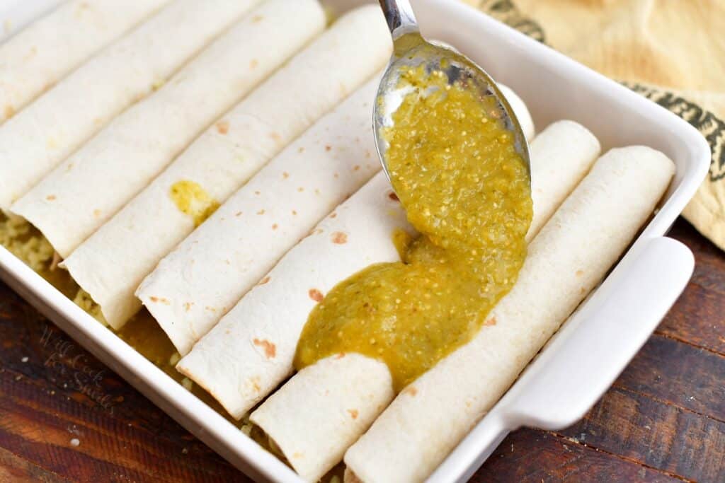 tomatillo sauce being spooned over uncooked chicken enchiladas