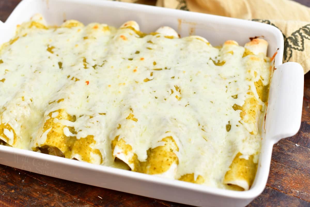 baked chicken enchiladas covered in green sauce and melted cheese in a white casserole dish
