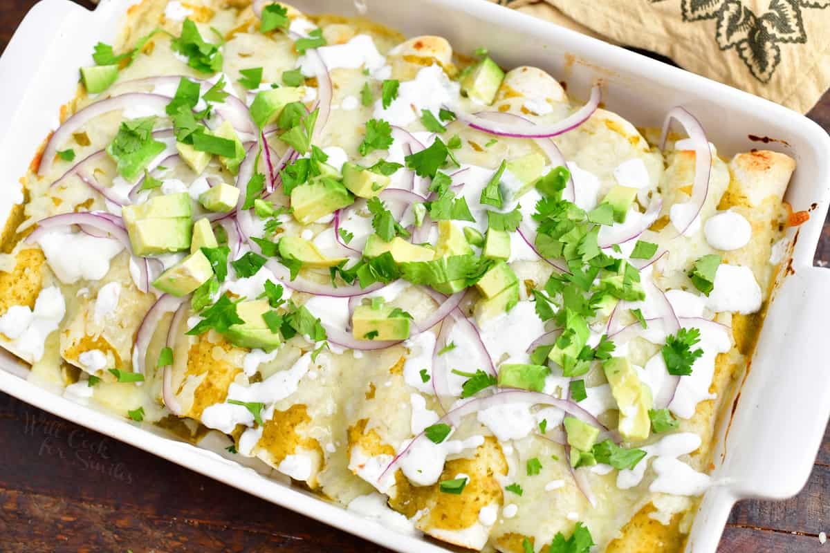 cooked pan of enchiladas verdes topped with red onion, avocado, and cilantro