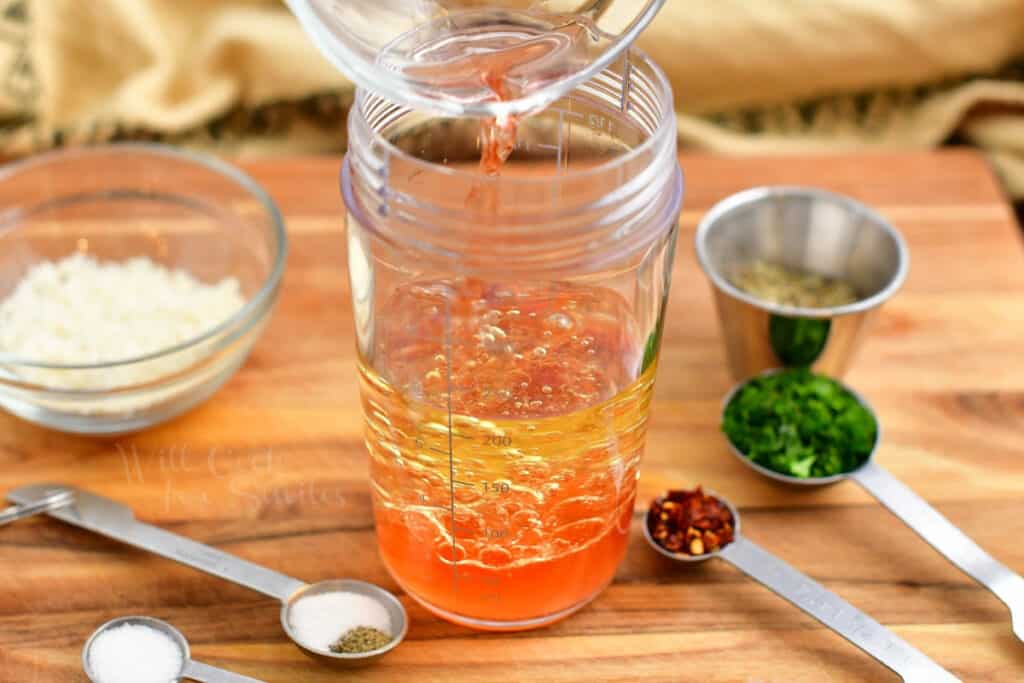 pouring red wine vinegar into mason jar with oil