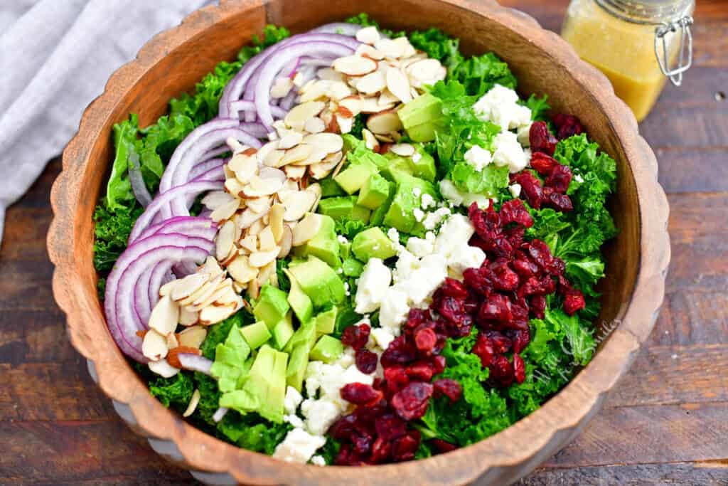 wooden bowl of kale salad with ingredients arranged in rows on top