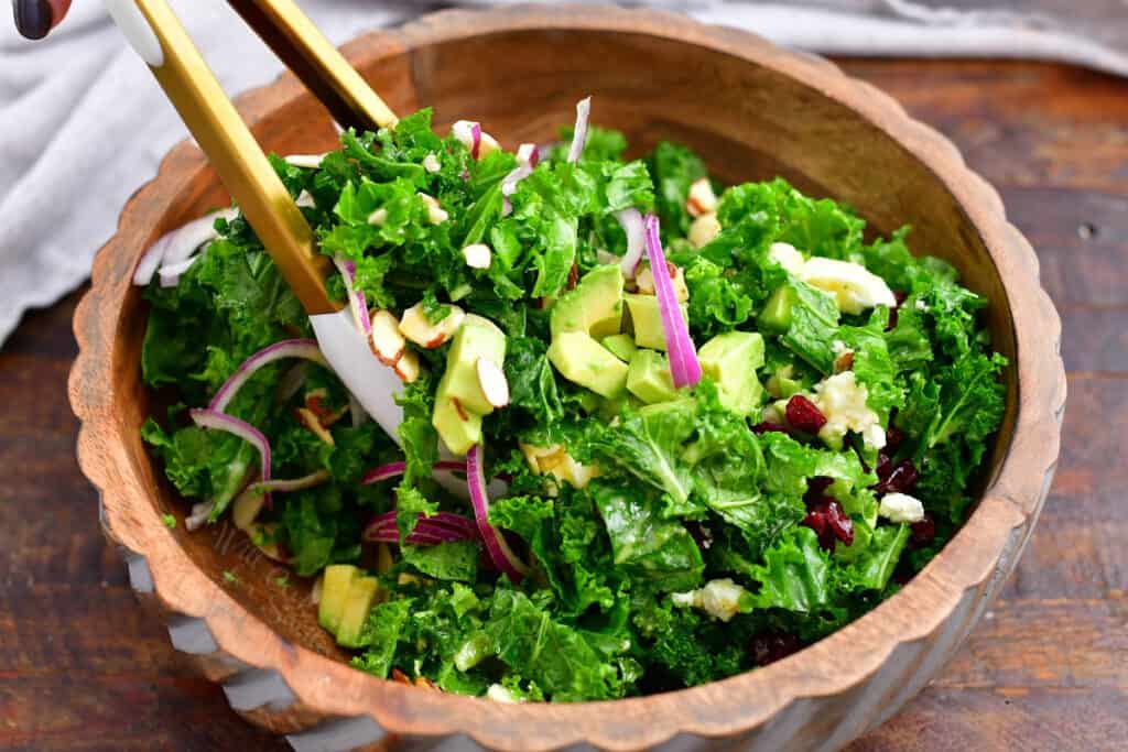 using wooden tongs to toss fresh kale salad before serving