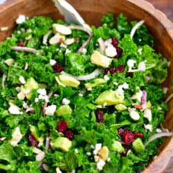 kale salad with almonds, avocado, dried cranberries, and feta cheese in wooden bowl