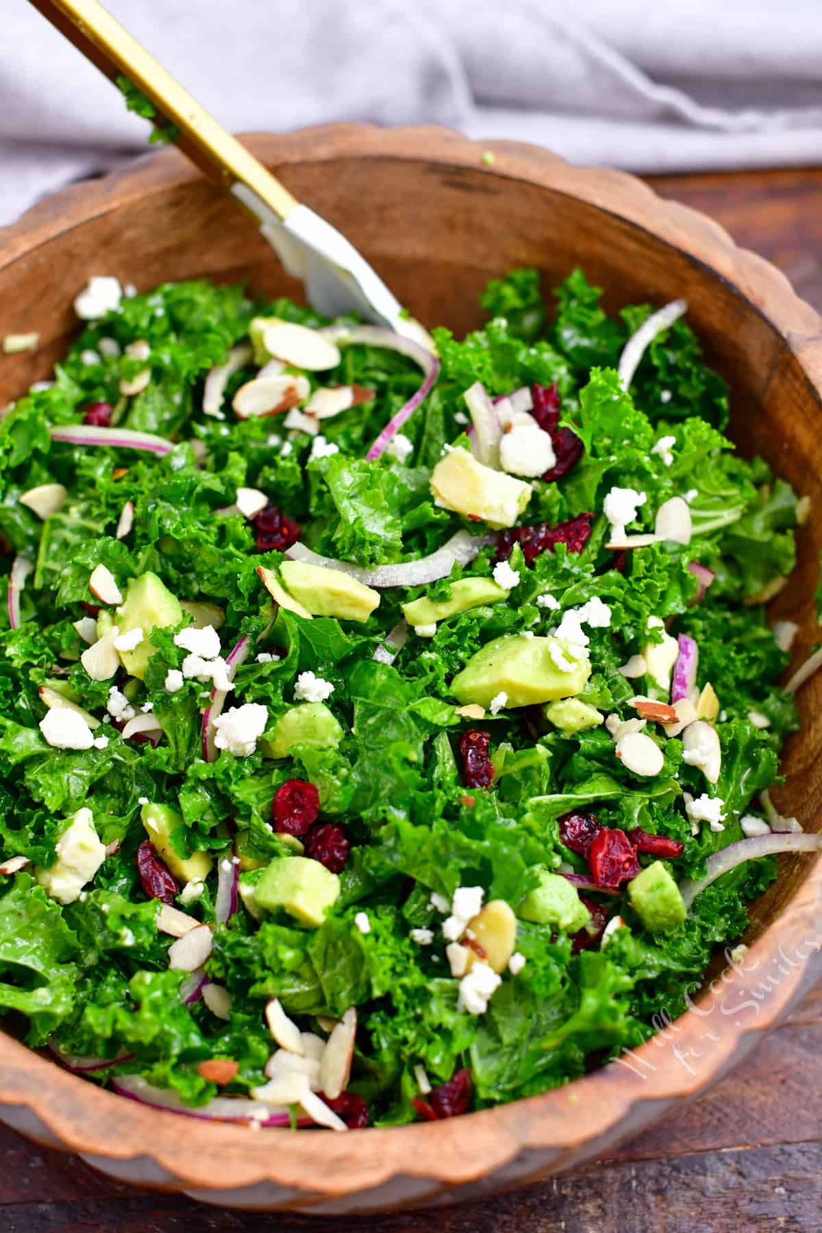 kale salad with almonds, avocado, dried cranberries, and feta cheese in wooden bowl