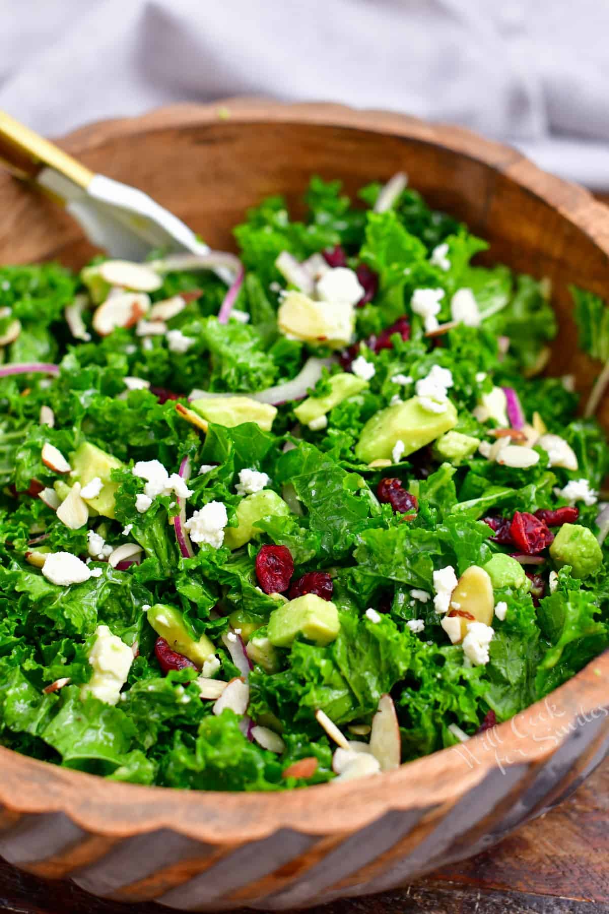 large wooden bowl of green salad with nuts, cheese, onion, and avocado