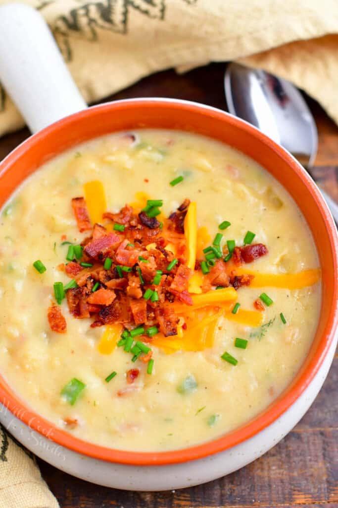 overhead of loaded baked potato soup with toppings sits next to a spoon and patterned kitchen towel
