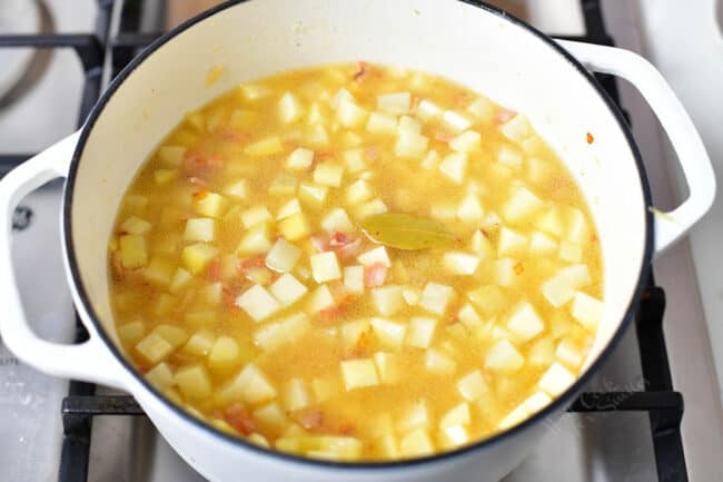 pot of cubed potatoes, bacon, broth, and a bay leaf in a pot on the stove