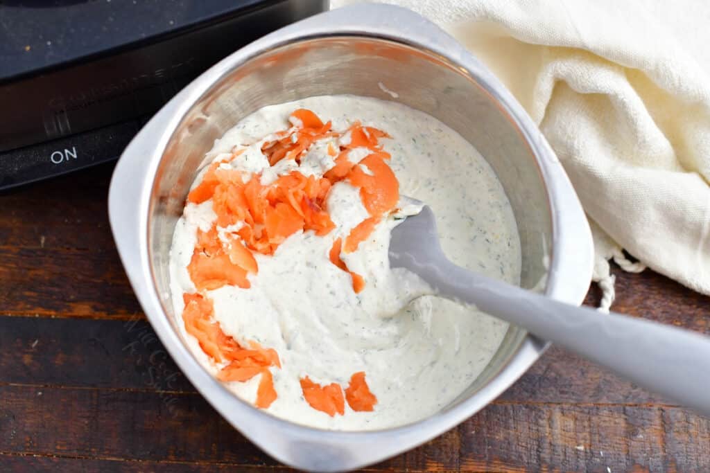 overhead image: stirring flaky pieces of salmon into a metal container of sour cream dip