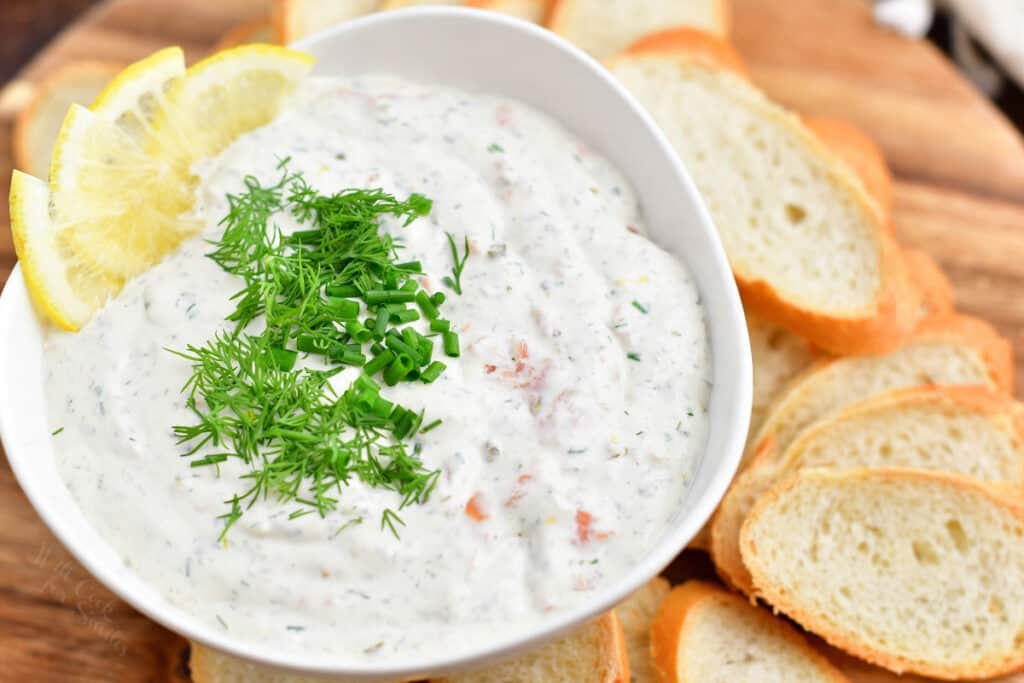close up image: salmon appetizer dip in white bowl with fresh dill and lemon garnish