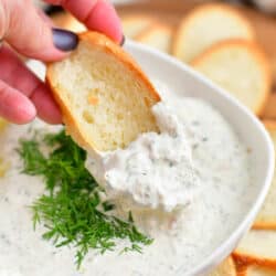 close up image: dipping toasted bread into bowl with salmon cream cheese dip
