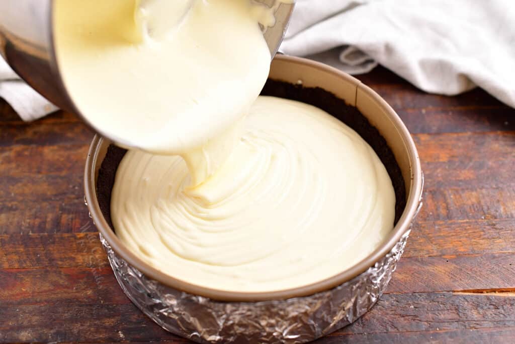 cheesecake filling being poured over Oreo cookie crust in a springform pan