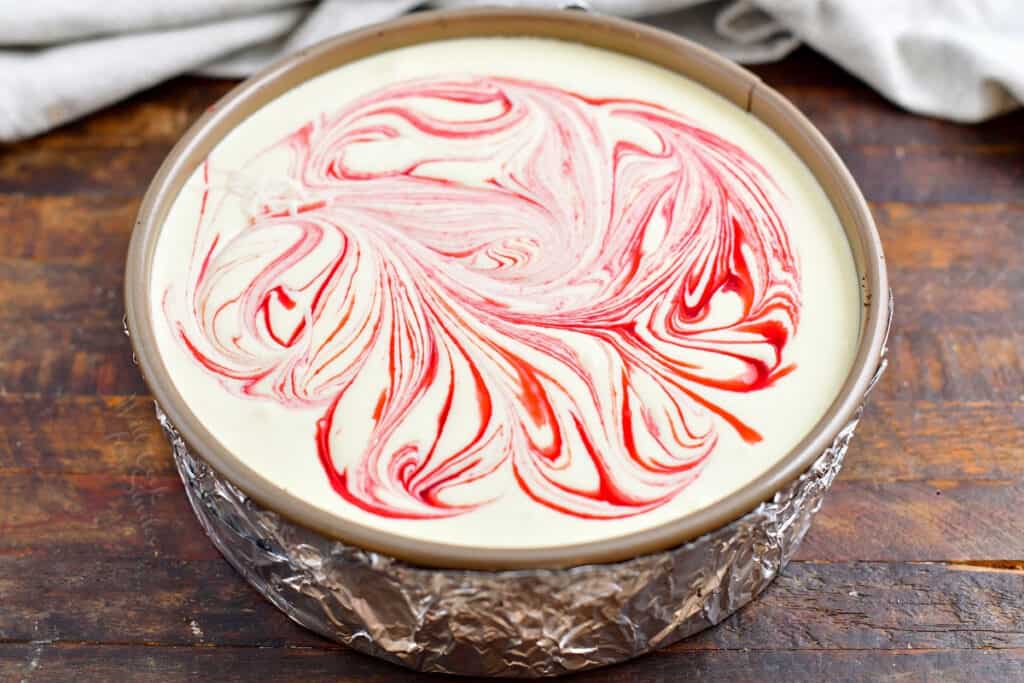 white chocolate cheesecake filling swirled with raspberry sauce in a springform pan with foil around the outside