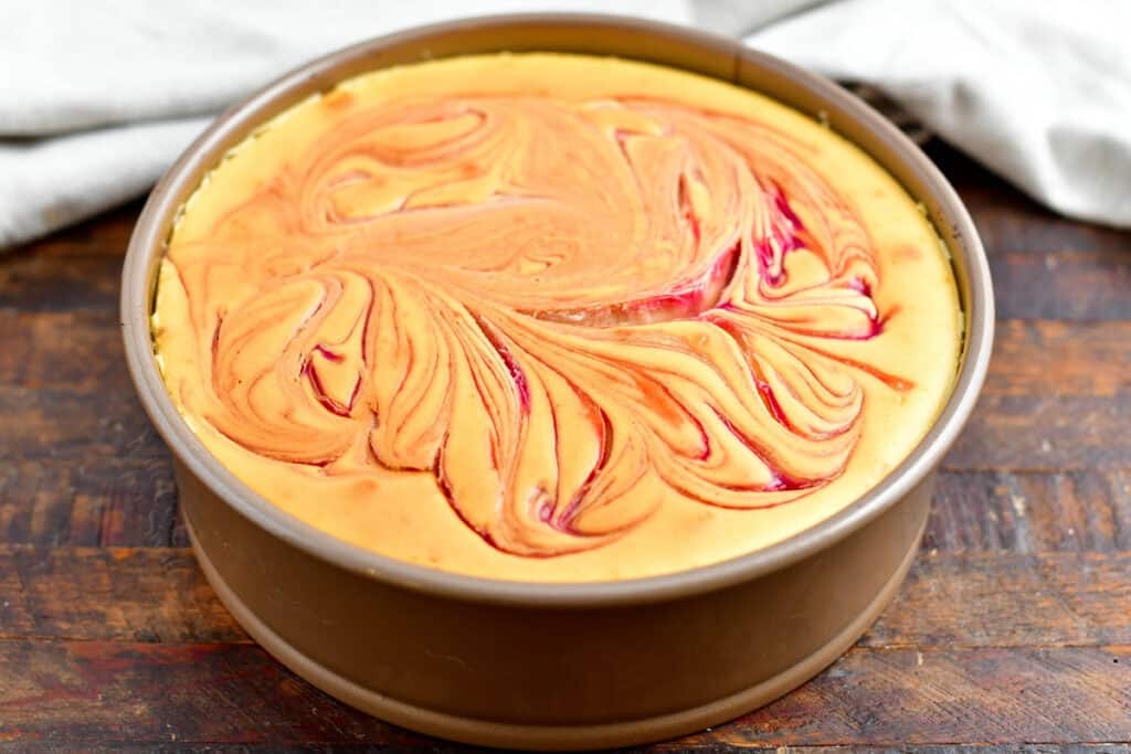 baked cheesecake with raspberry swirls in a springform pan on a wooden surface