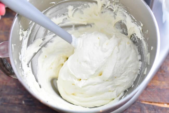closeup: cream cheese frosting being mixed in a large bowl with a spatula
