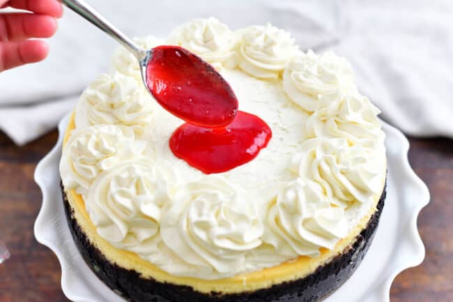 raspberry sauce being spooned on top of a white chocolate cheesecake with Oreo crust