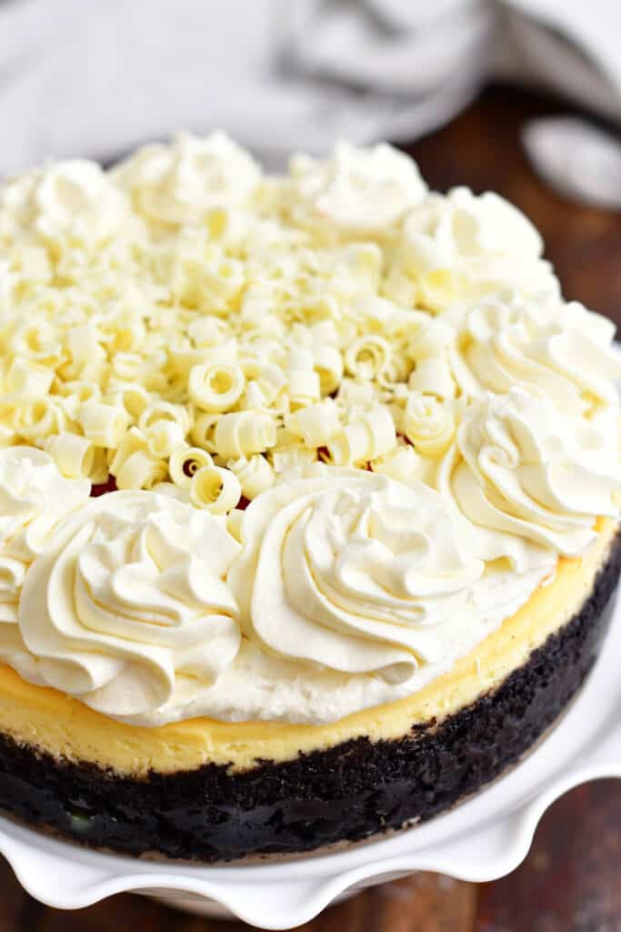 whole cheesecake with Oreo crust topped with frosting and white chocolate shavings