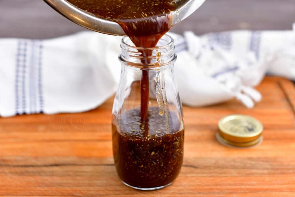 balsamic vinaigrette being poured from a metal bowl into a glass jar