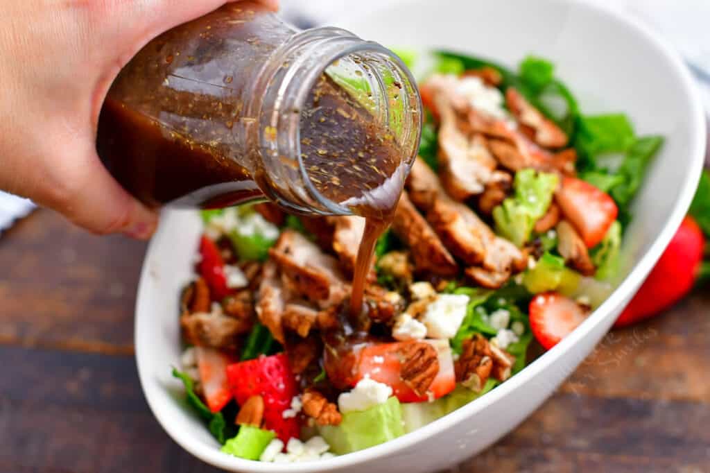 jar of balsamic vinaigrette being poured over a green salad with chicken