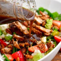 balsamic dressing being poured over a salad topped with chicken