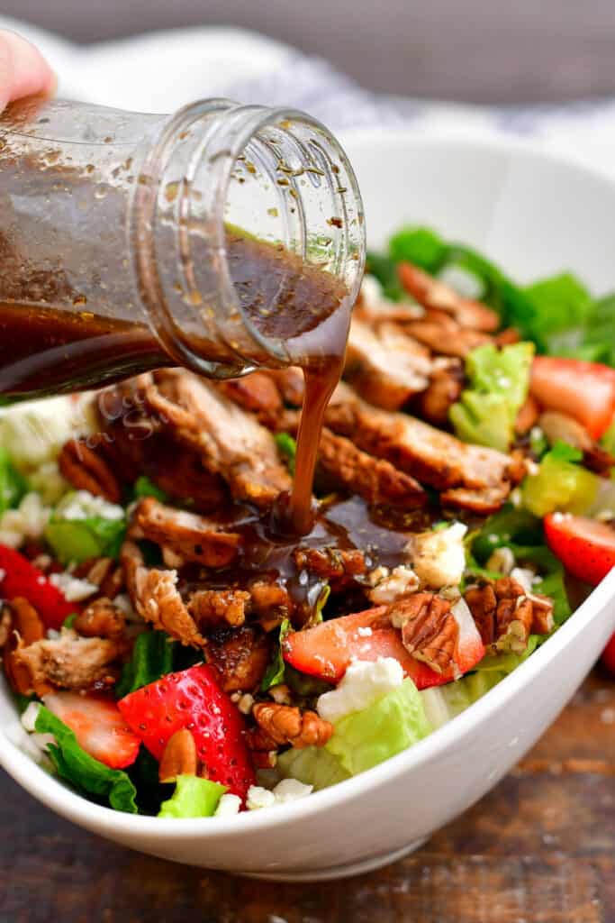 balsamic dressing being poured over a salad topped with chicken