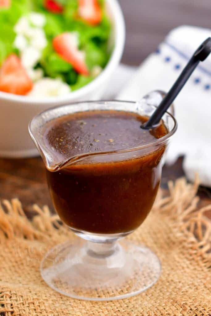 glass container of salad dressing in a glass serving cup with ladle