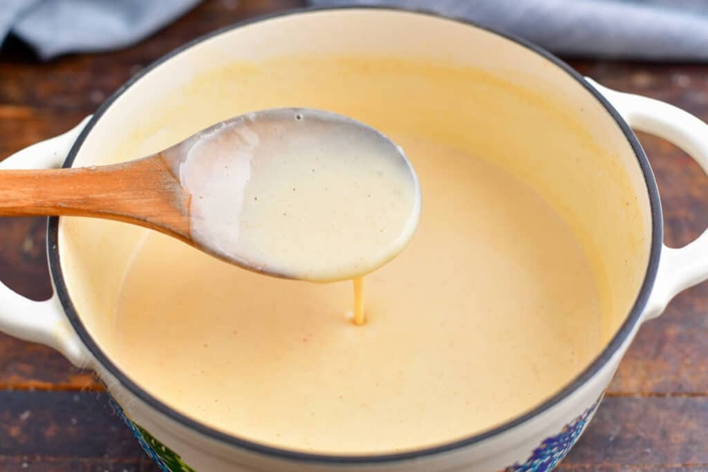 beer cheese sauce on wooden spoon above saucepan