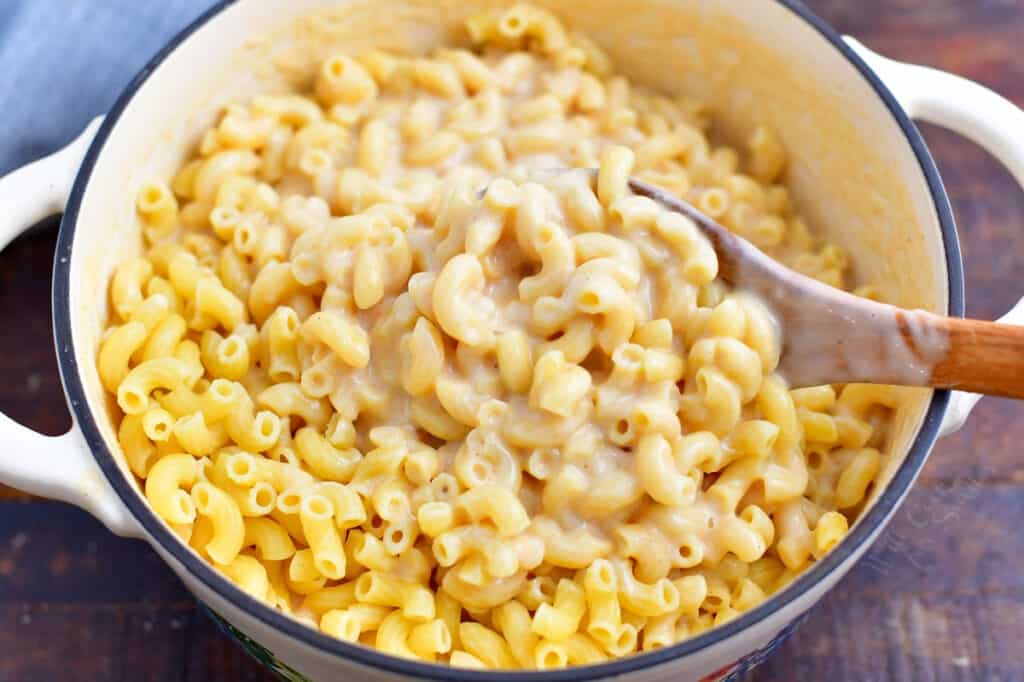 wooden spoon stirring sauce into a pot of elbow pasta