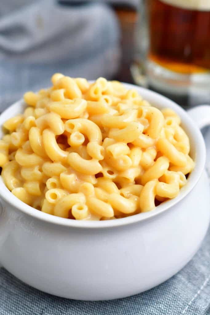 white soup bowl filled with beer cheese mac and cheese on a grey towel in front of a mug of beer