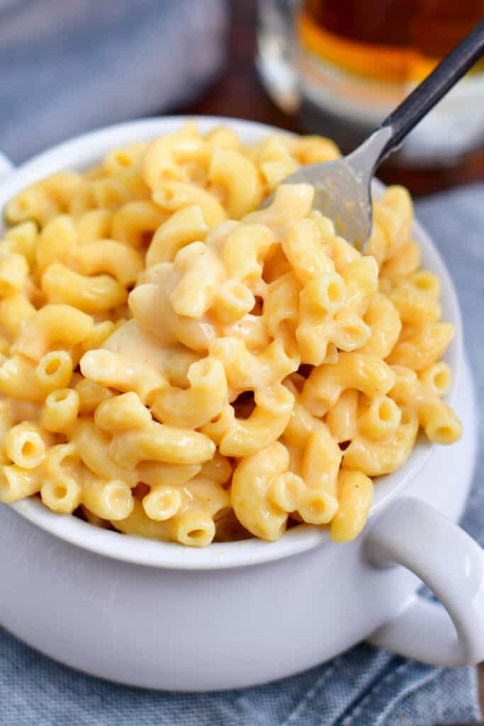 fork lifting creamy beer cheese sauce mac and cheese out of white soup crock