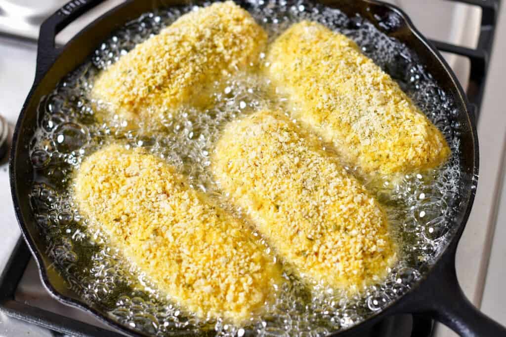 panko coated chicken breasts cooking in skillet of oil