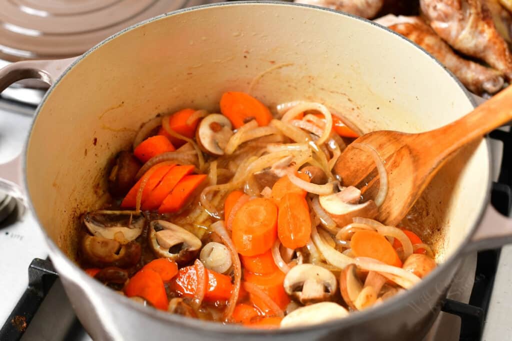 wooden spoon stirring vegetables in a dutch oven on the stove