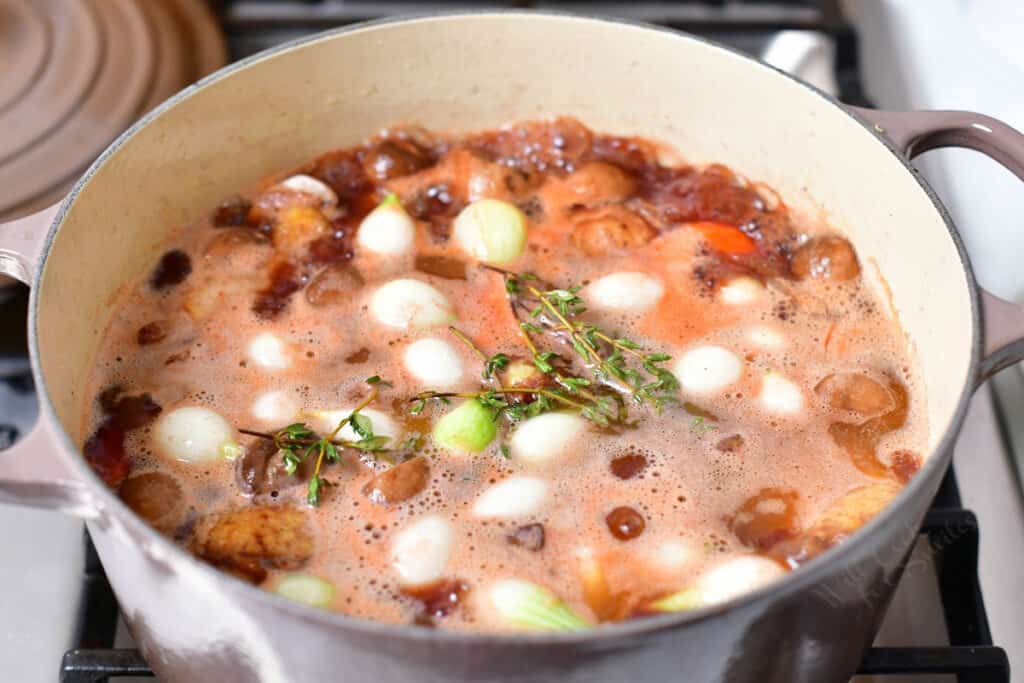 coq au vin simmering in a pot on the stove