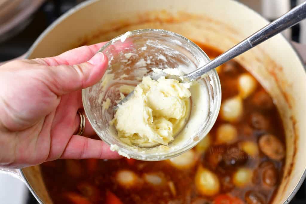 flour and butter being mixed in a small ball over a pot of coq au vin