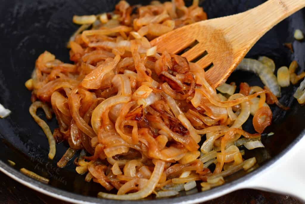 wooden spoon stirring caramelized onions in a skillet