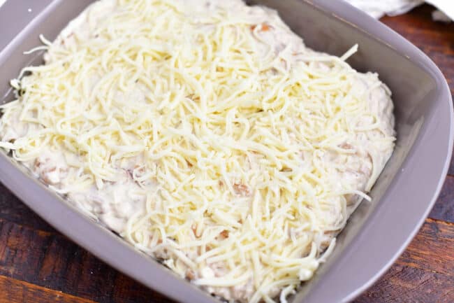 grey baking dish with creamy white mixture topped with white shredded cheese